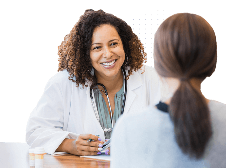 Smiling female doctor with a stethoscope around her neck talking to a female patient across the desk in a medical consultation